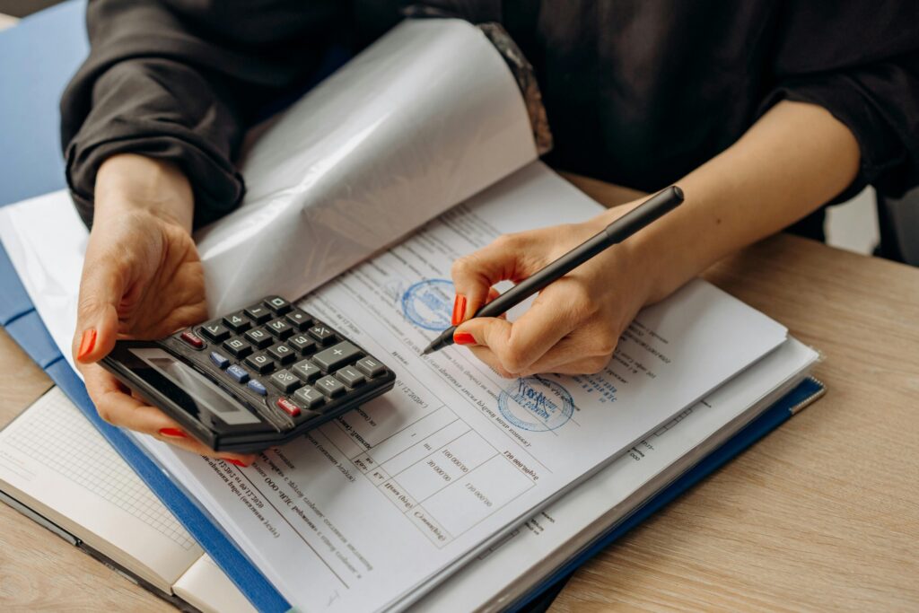 pexels photo 8296977 8296977 An accountant using a calculator and signing paperwork, showcasing financial analysis.